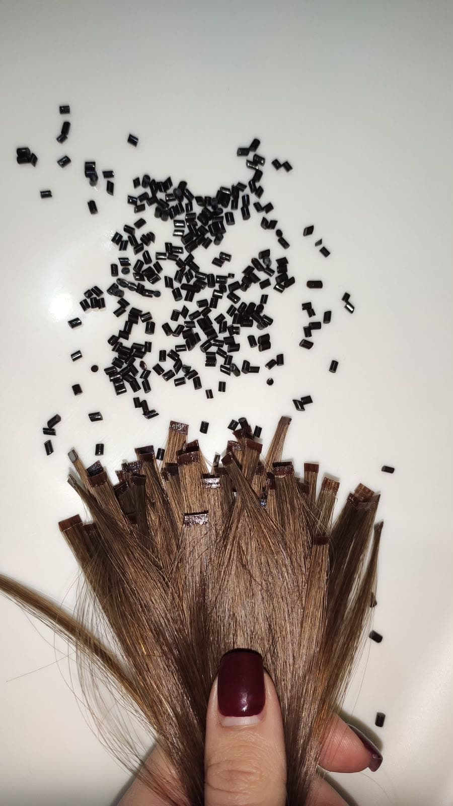 Keratin Bond strands held in the hand beside loose keratin granules